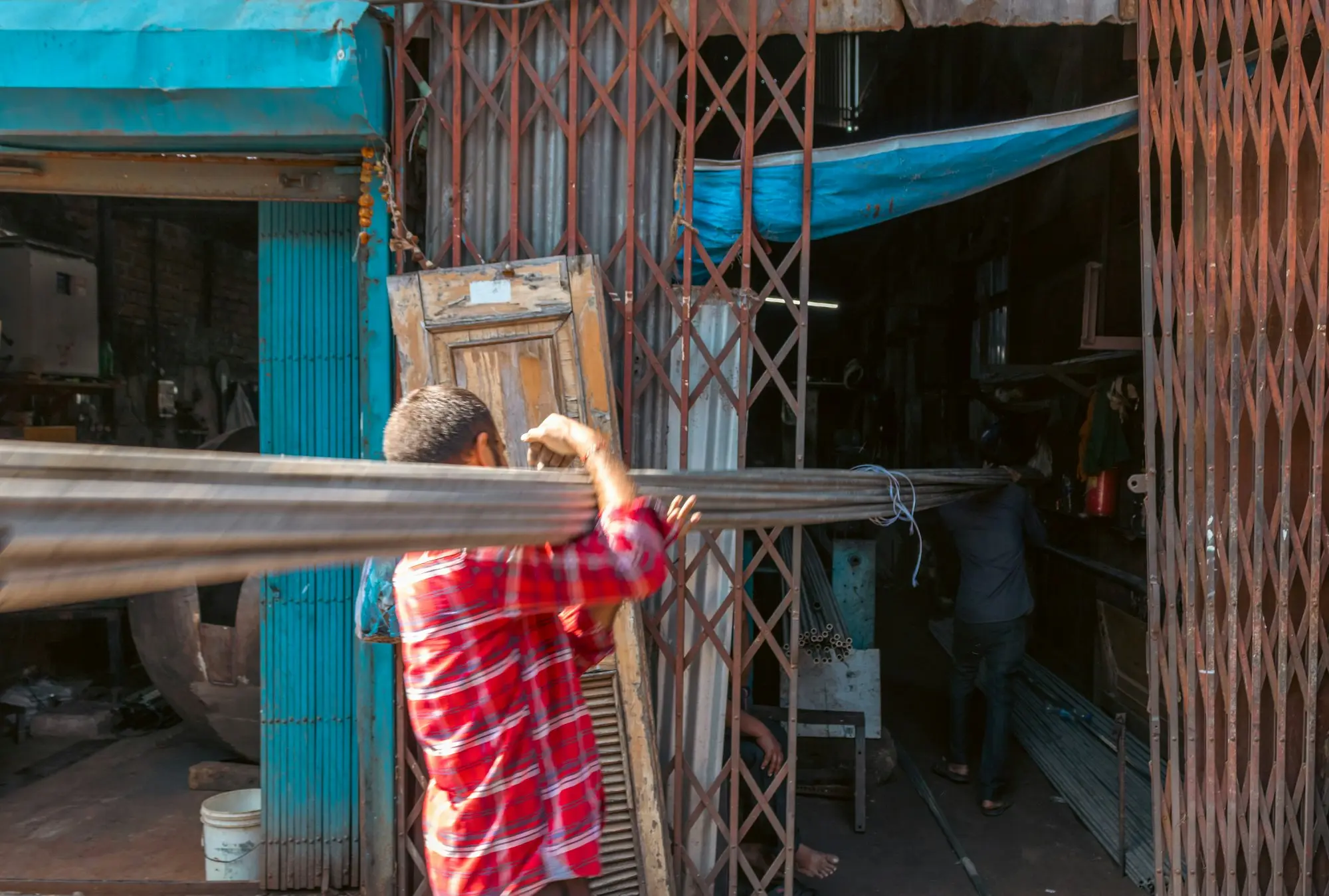 A tradesman carrying metal poles into a shop, work that waits when funding is slow